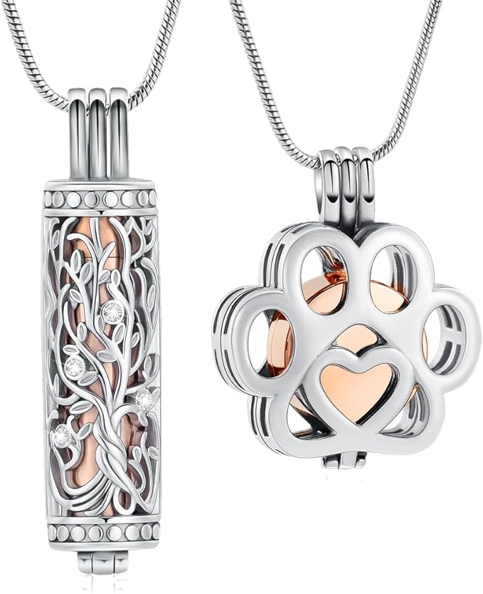 Se muestran dos colgantes de joyas conmemorativas. El primero tiene forma cilíndrica, con acabado en plata y un grabado detallado del árbol de la vida y pequeños puntos brillantes. El segundo tiene forma de huella de pata de mascota con un corazón hueco en el centro, con un acabado en oro rosa. Ambos están colgando de cadenas finas, preparados para llevar cerca del pecho.